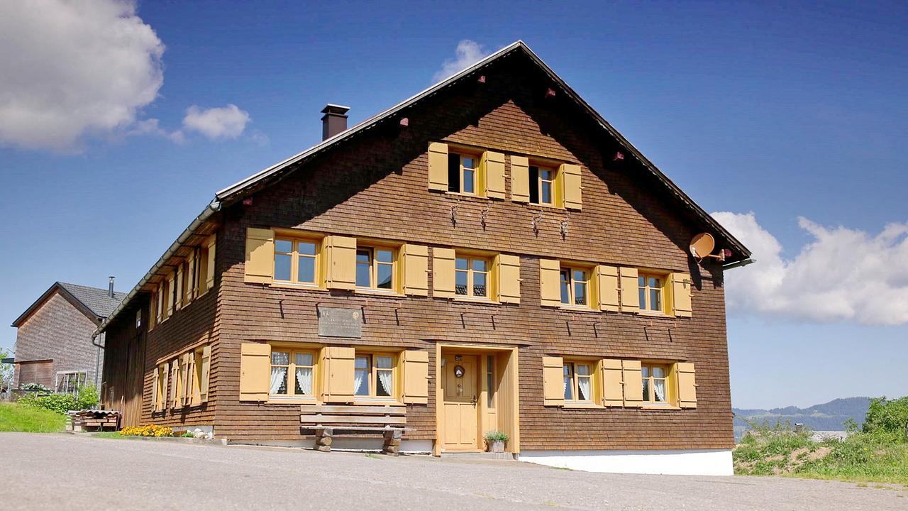 © ORF Das Hermann-Gmeiner-Geburtshaus, ein traditionelles Holzhaus mit gelben Fensterläden in Alberschwende