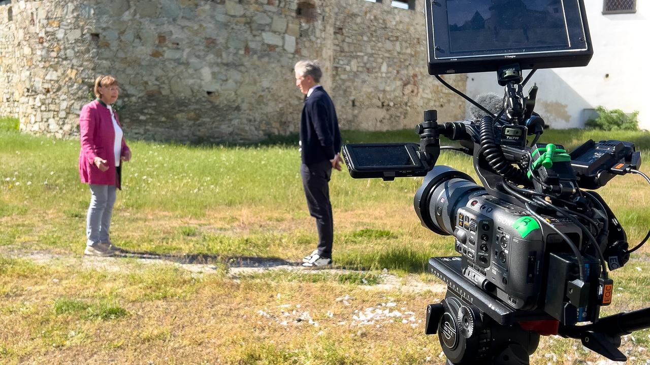 © ORF/Interspot/Philip Pürcher, Carlo Hofmann Eine professionelle Kamera im Vordergrund filmt Johann-Philipp Spiegelfeld und Anna Schlanitz-Bolldorf, die vor dem Schlossturm stehen.