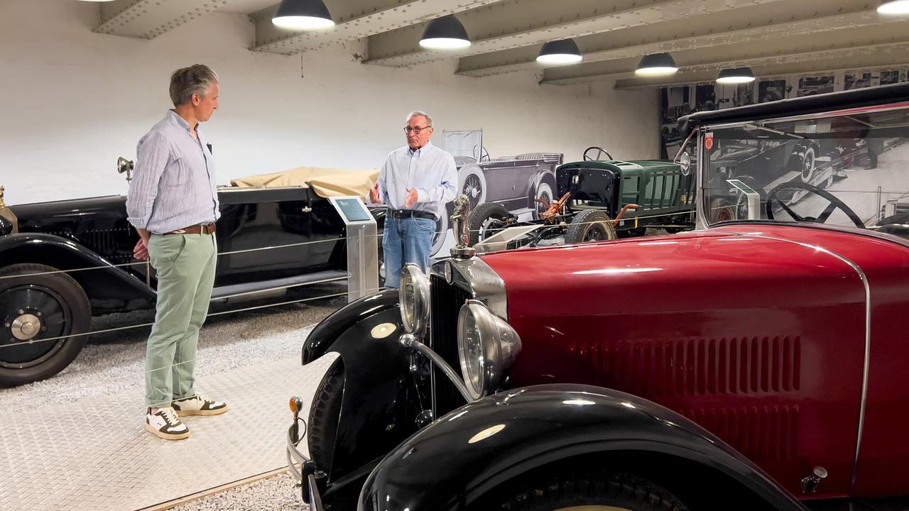 Johann-Philipp Spiegelfeld und Wolfgang Boesch unterhalten sich in einer Halle mit Oldtimern zwischen den historischen Autos.