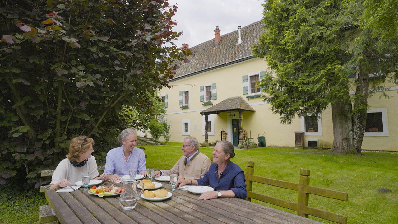 Bernadette Boesch, Johann-Philipp Spiegelfeld, Wolfgang Boesch und Marianne Boesch-Leibrecht sitzen beim Essen am Gartentisch vor dem Burggebäude.