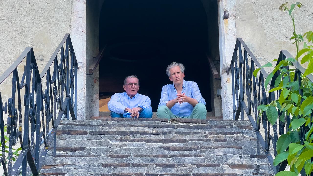 Wolfgang Boesch und Johann-Philipp Spiegelfeld sitzen beim Eingang einer Burgmauer vor einer Steintreppe.