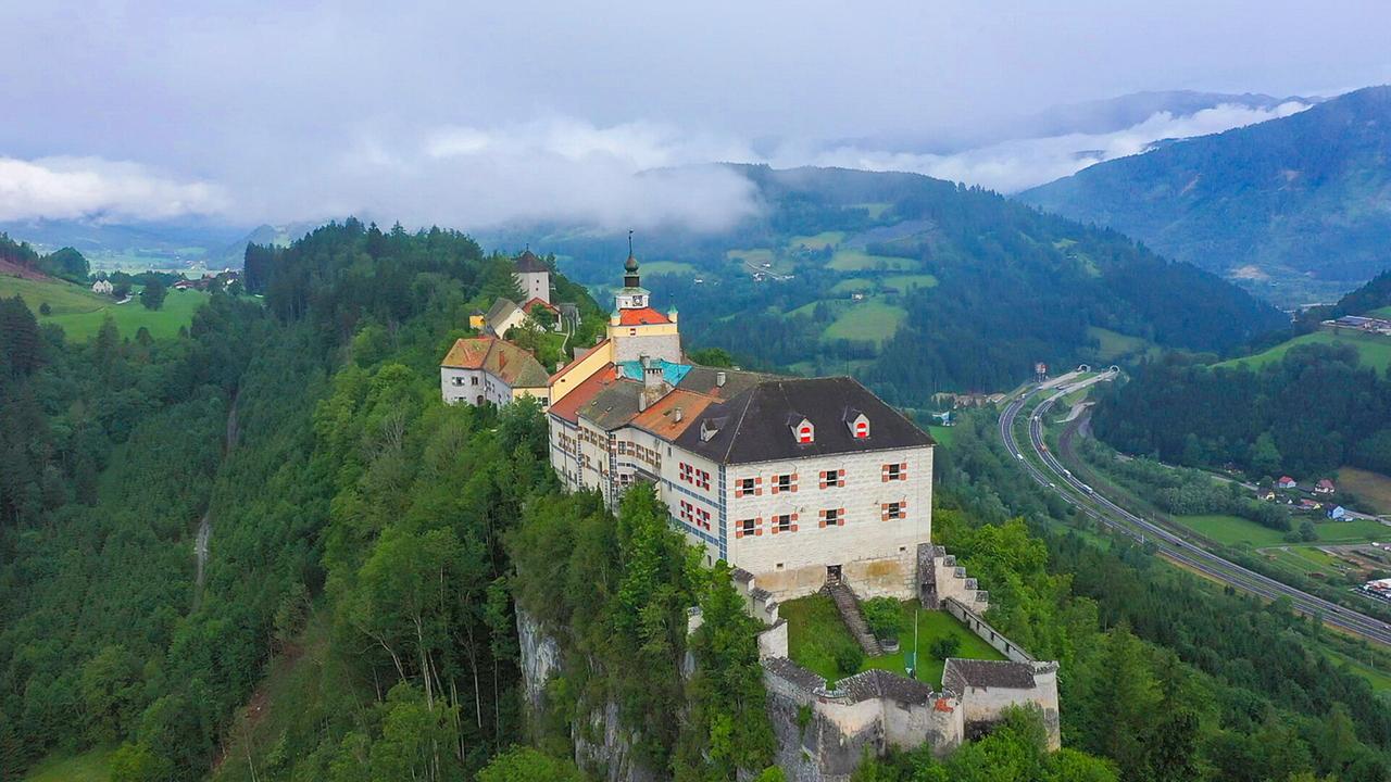 Luftaufnahme von Burg Strechau über einem Tal mit Autobahn und Tunneln, umgeben von bewaldeten Hügeln.