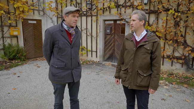 Johann-Philipp Spiegelfeld steht mit Carl-Philip Clam-Martinic im Freien vor einer mit Weinreben bewachsenen Gebäudefassade.