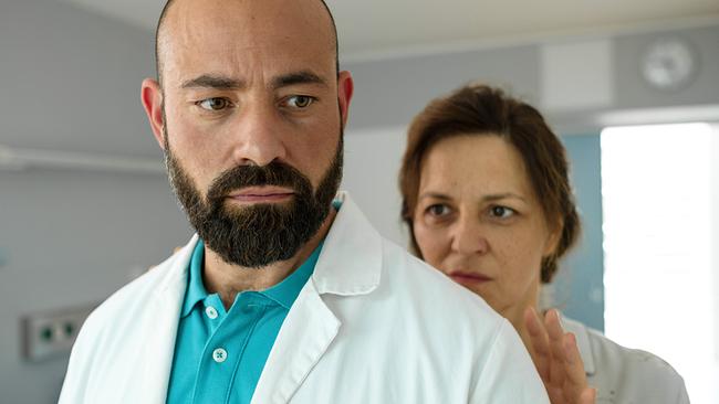 © ORF/BR/ Lotus Film/Petro Domenigg Dr. Paul Hoffmann im Arztkittel blickt ernst nach vorne. Hinter ihm steht Patientin Caroline Binder und möchte ihm eine Hand auf seine Schulter legen.
