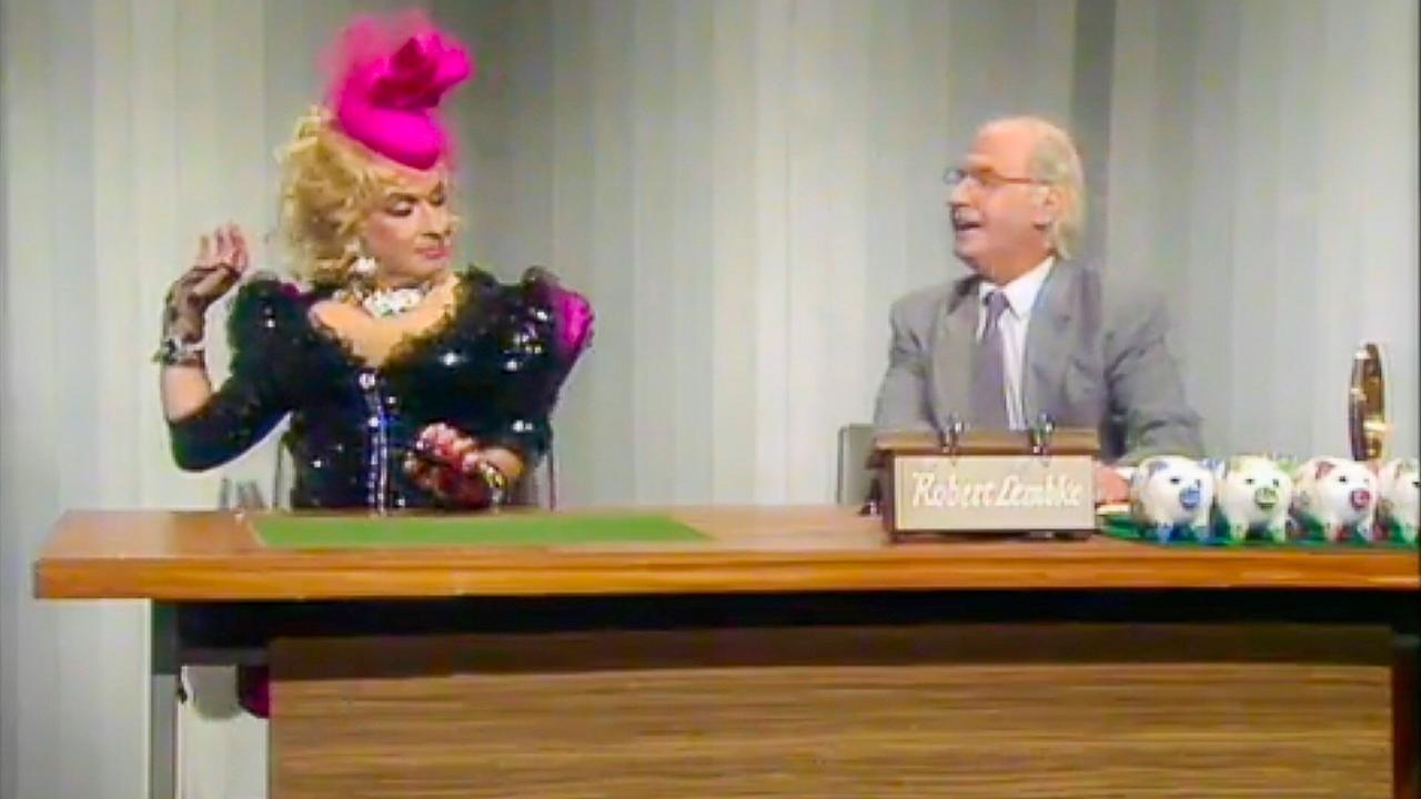 © ORF Der doppelte Peter Alexander sitzt an einem Fernsehschreibtisch, einmal als extravagant gekleidetes Modell gestikuliert und einmal als Robert Lembke beim Beruferaten (Was bin ich?).