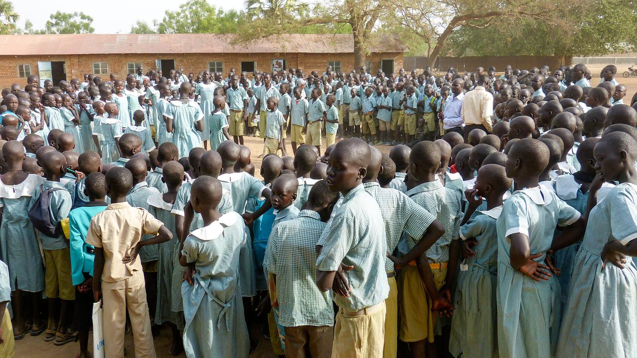 © ORF/FOR TV Eine große Gruppe von Schulkindern in Uniformen steht im Freien in einem Kreis auf einem Schulhof in Afrika.