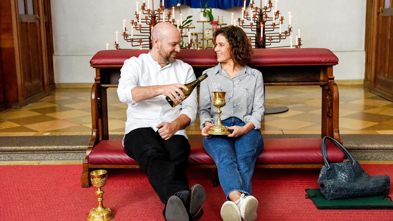 "Himmel, Herrgott, Sakrament – Der richtige Mann": Pfarrer Reiser (Stephan Zinner) und Lisa (Anne Schäfer) trinken Wein und reden.