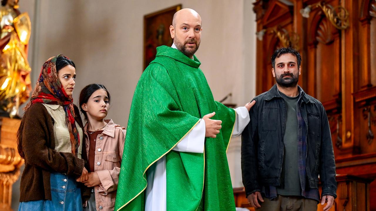 © ORF/BR/maze pictures GmbH/Barbara Bauriedl Hans Reiser in grünem Messgewand steht mit der syrische Flüchtlingsfamilie Aboud in der Kirche und greift Shamun Aboud freundschaftlich auf die Schulter