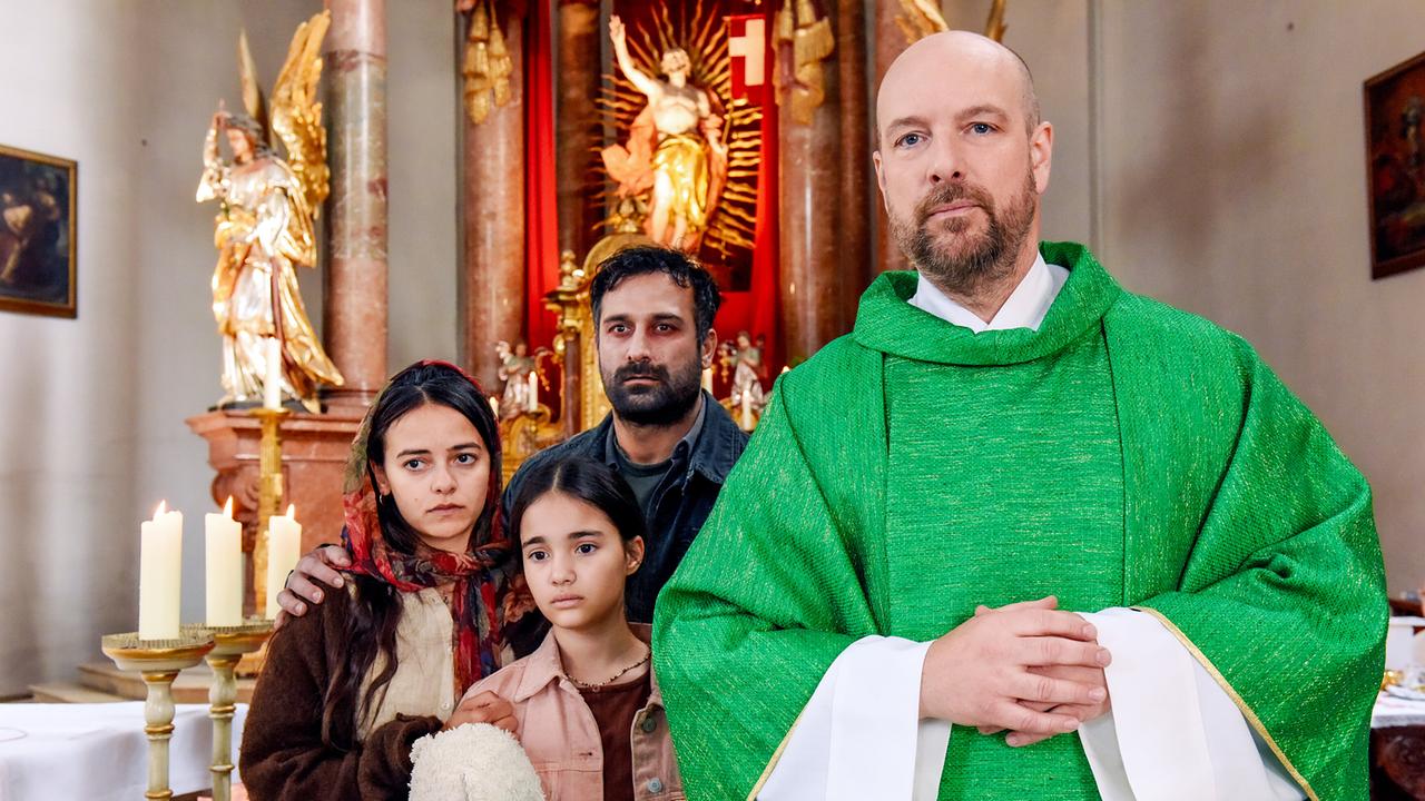 © ORF/BR/maze pictures GmbH/Barbara Bauriedl Hans Reiser in grünem Messgewand steht in der Kirche mit der syrische Flüchtlingsfamilie Aboud, die ängstlich nach vorne blickt.
