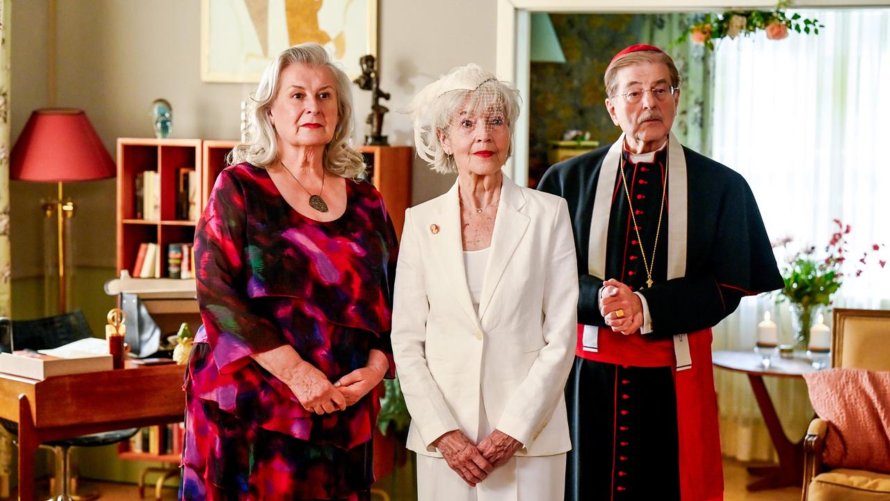 © ORF/BR/maze pictures GmbH/Barbara Bauriedl Gertrud Hartberger in einem Kleid, Irmi Brunnenmayr im weißen Anzug und mit weißem Haarschmuck und Kardinal Brunnenmayr stehen nebeneinander in einem hellen Wohnraum.
