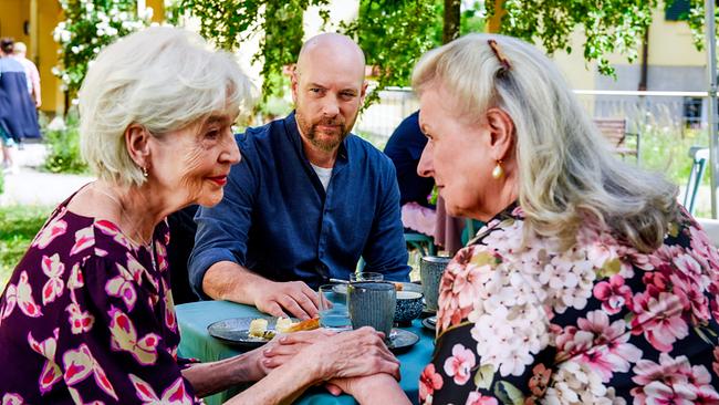 © ORF/BR/maze pictures GmbH/Barbara Bauriedl Die zwei ältere Frauen Irmi Brunnenmayr und Gertrud Hartberger sitzen sich in einem Gastgarten gegenüber, halten sich an den Händen, während Hans Reiser am Tisch ihnen aufmerksam zusieht.
