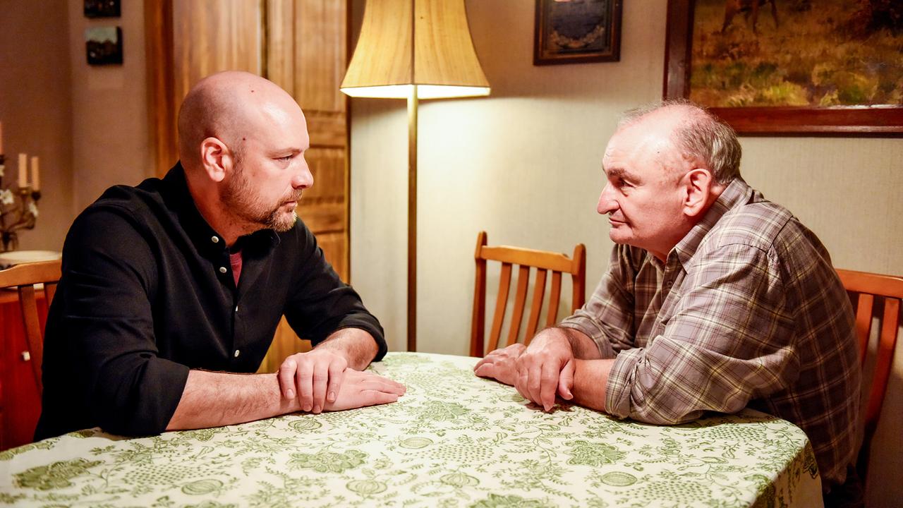 © ORF/BR/maze pictures GmbH/Barbara Bauriedl Hans Reiser unterhält sich mit seinem Vater an einem Esstisch in einem warm beleuchteten Zimmer.