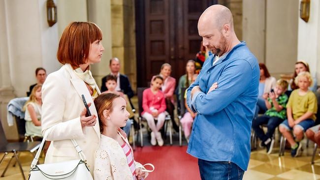 © ORF/BR/maze pictures GmbH/Barbara Bauriedl In einem Gemeindesaal stehen sich Heike Mühlbauer mit der kleinen Georgina und Hans Reiser in blauem Hemd bei einem Erstkommunionstreffen angespannt gegenüber.