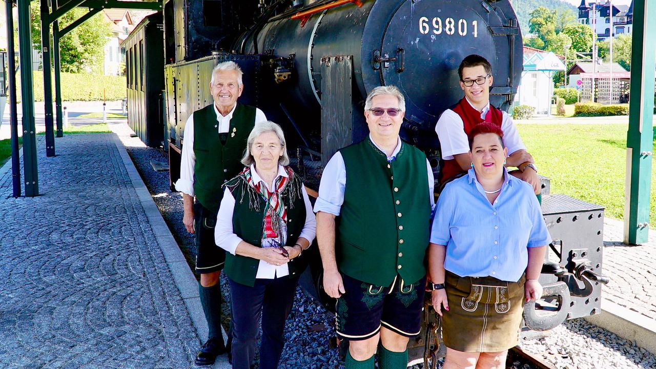 © ORF/DEGN FILM/Barbara Meikl 3 Generationen der Eisenbahnerfamilie Deopito: 1.Generation: Alfred und Anna Deopito (links), 2. Generation: Ludwig und Daniela Deopito (mitte) mit Sohn Dominik Deopito (rechts hinten) in der 3. Generation stehen vor der historischen Dampflok 69801 an einem überdachten Bahnsteig.