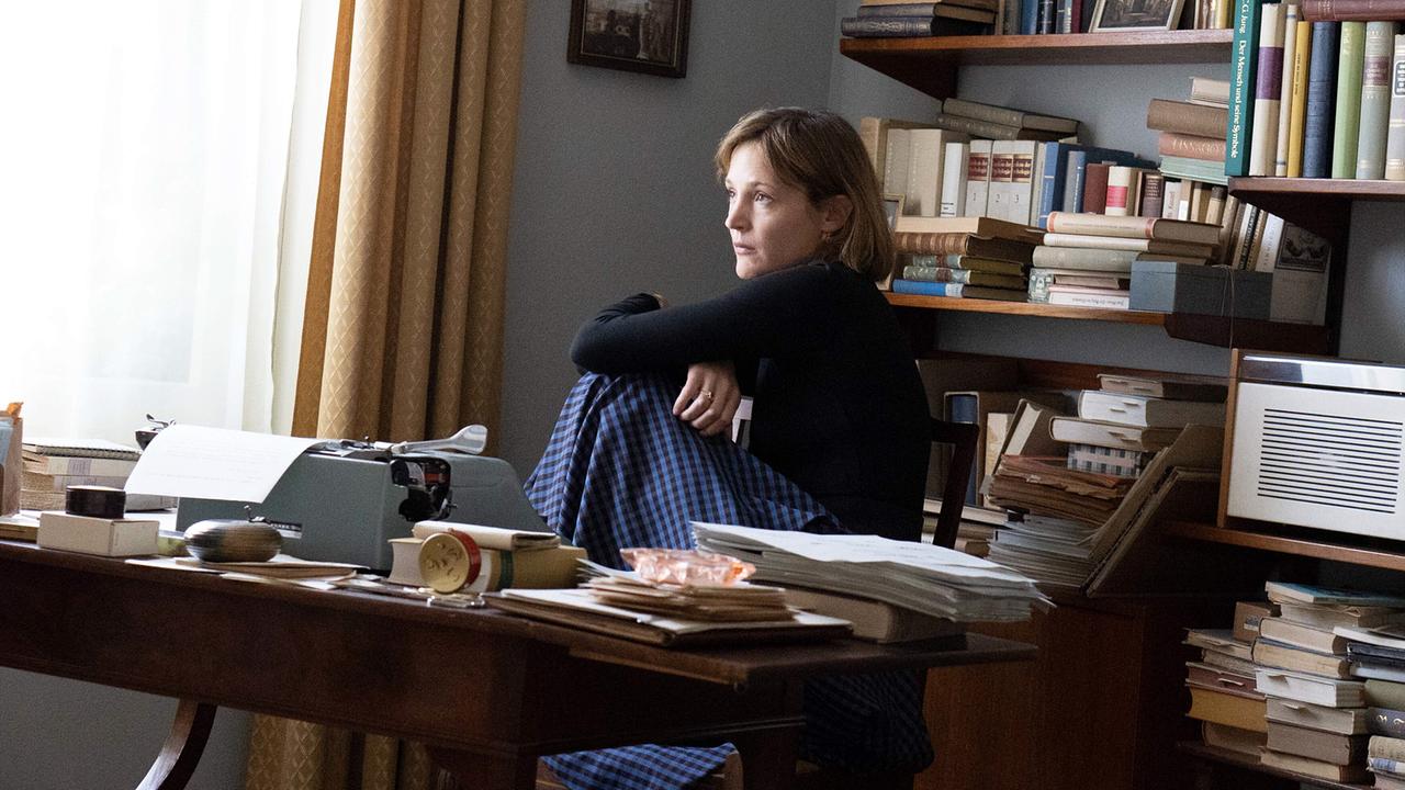 Vicky Krieps als Ingeborg Bachmann sitzt nachdenklich an einem Schreibtisch in einem Arbeitszimmer voller Bücher und Papiere.