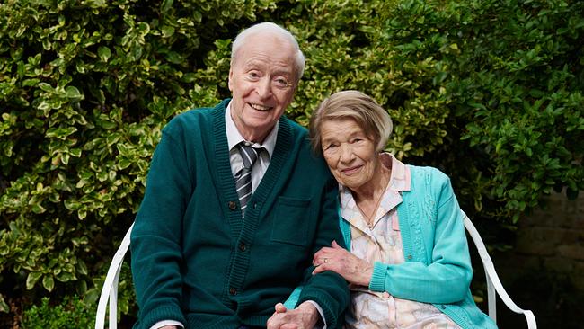 © ORF/LEONINE Studio/Rob Youngson Michael Caine als Bernard Jordan und Glenda Jackson als Irene Jordan sitzt lächelnd eng beieinander auf einer Gartenbank vor einer dichten grünen Hecke.