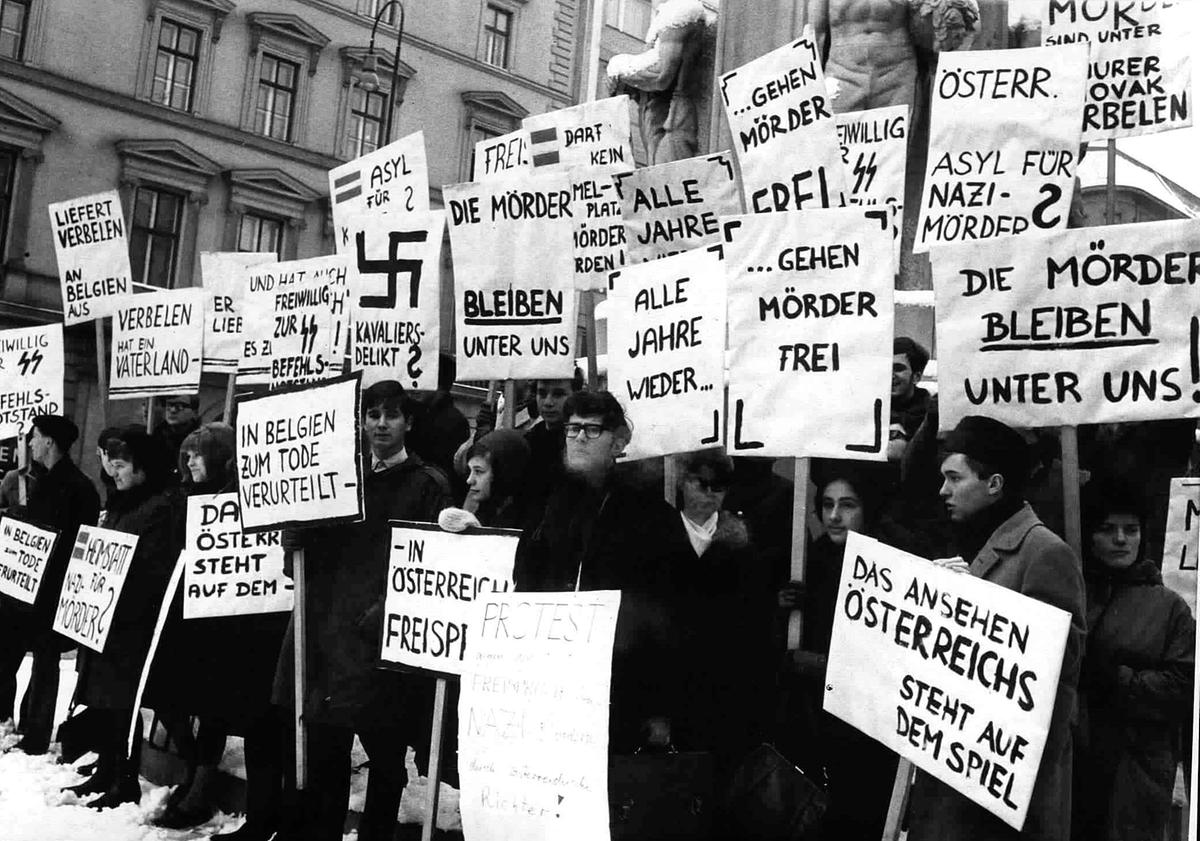 Eine historische Schwarzweißaufnahme zeigt Studenten mit Transparenten und Plakaten bei einer politischen Demonstration gegen den Freispruch von Jan Verbelen 1965