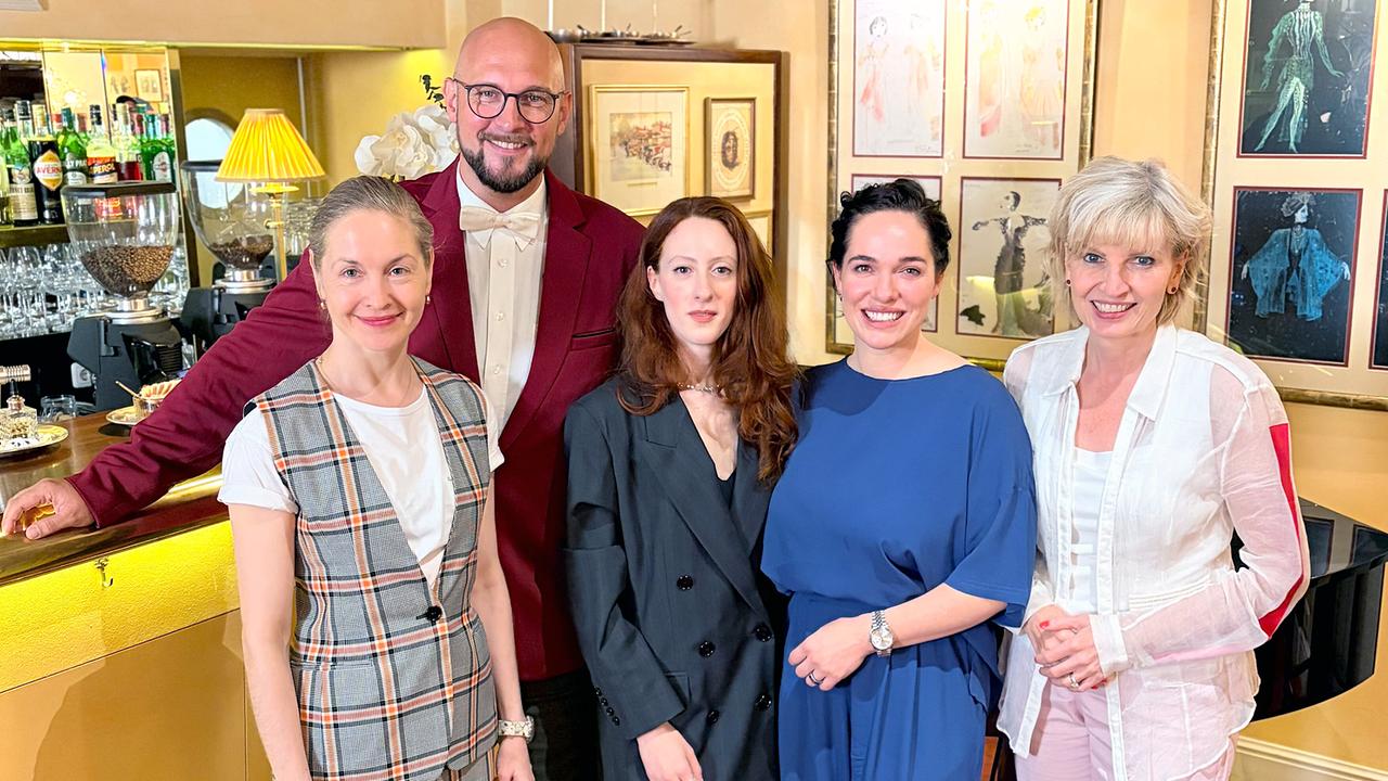 © ORF/Landesstudio Salzburg „Der Club der Buhlschaften“ – Verena Altenburger, Valery Tscheplanowa sowie die heurige Buhlschaft Roxane Duran – posiert mit Romy Seidl-Laux und einem Mann lächelnd in einem stilvoll eingerichteten Lokal vor einer Bar.