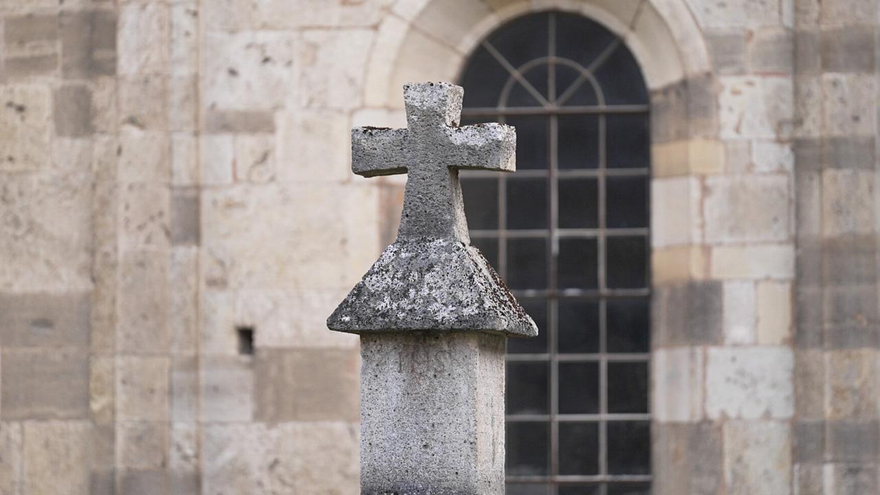 Steinkreuz vor einer alten Kirchenfassade mit Rundbogenfenster