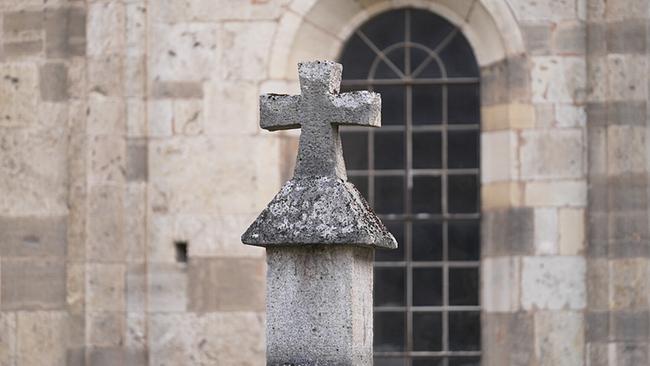 Steinkreuz vor einer alten Kirchenfassade mit Rundbogenfenster