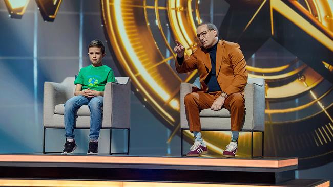 © ORF/NDR/Thorsten Jander Samuel (9) und Manuel Hobiger beim Ländergrenzen-Duell sitzen auf Sesseln auf einer Bühne mit goldenem Hintergrund.