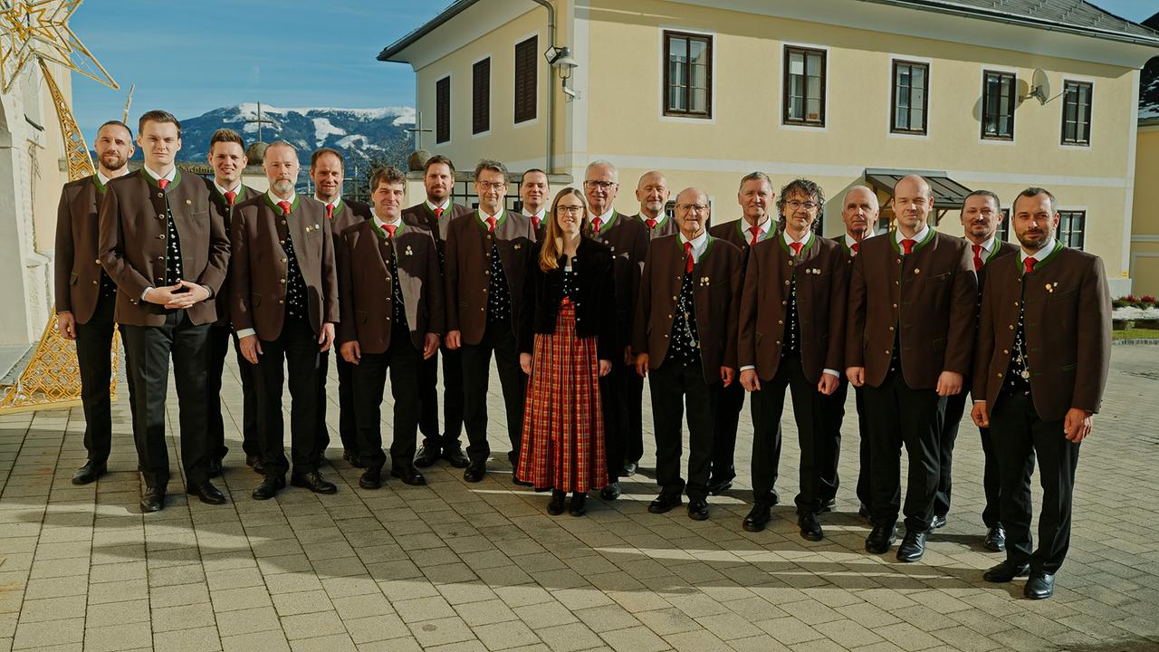 Gruppenfoto der Sängerrunde Zlan in Tracht auf einem Dorfplatz bei Sonnenschein