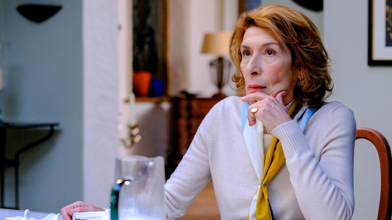 Constanze Laux sitzt nachdenklich am Esstisch in einem hellen Esszimmer, den Kopf auf die Hand gestützt.