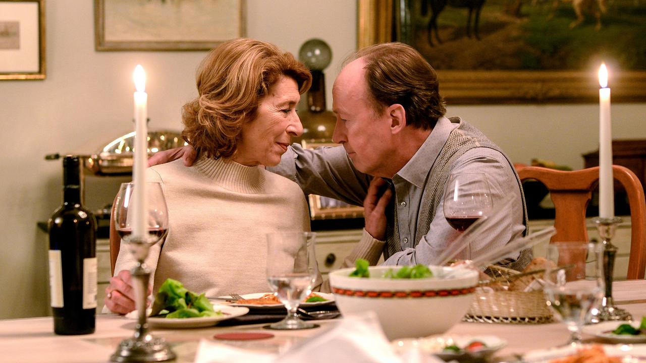 Am Esstisch sitzt Constanze Laux neben ihrem Mann, der sie umarmt, beim Abendessen bei Kerzenlicht. 