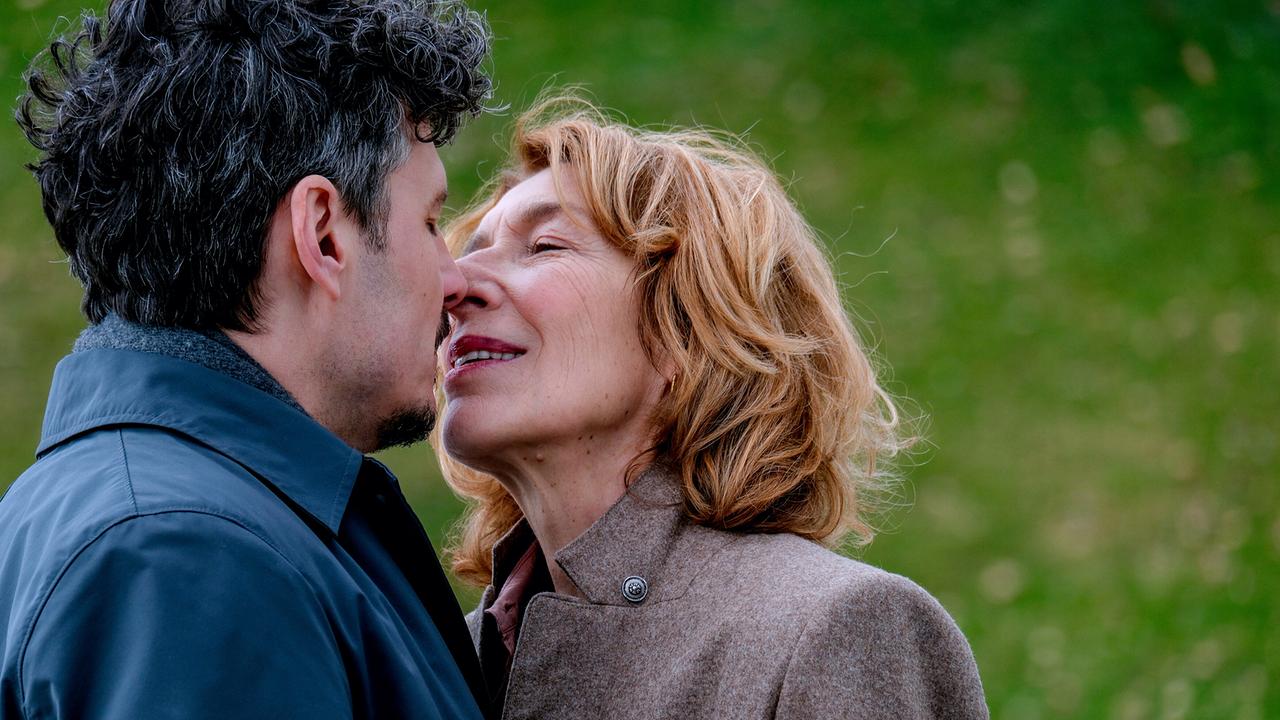 Ricardo Westerhoff und Constanze Laux stehen sehr nah beieinander im Park und küssen sich.