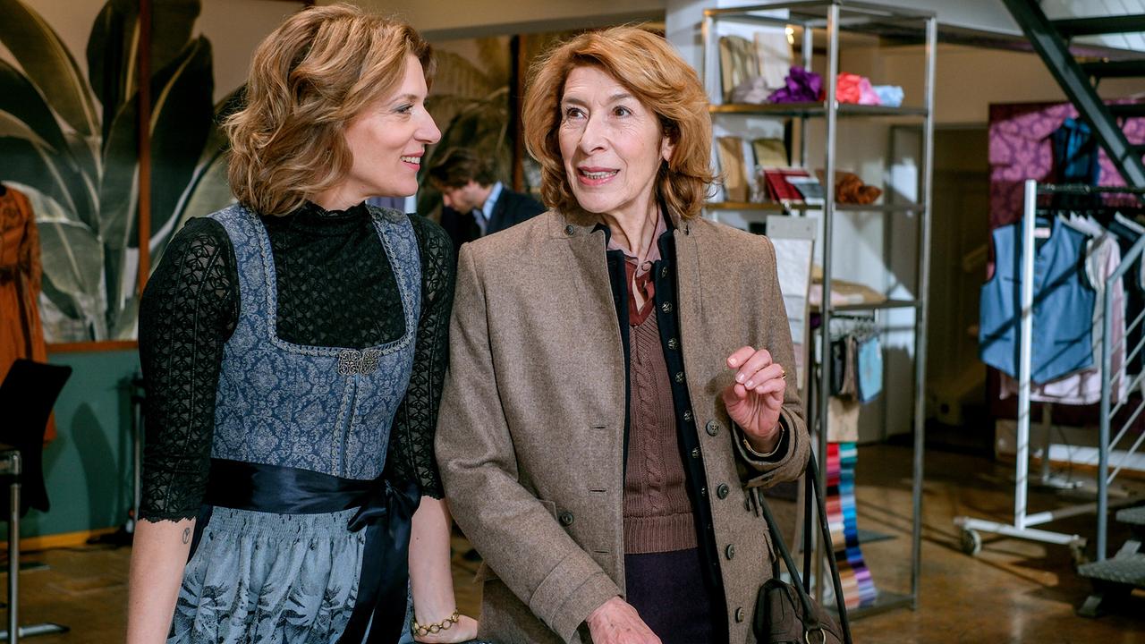 Karin Biederstädt und Constanze Laux stehen in einem Trachtenmodeatelier neben einem Zuschneidetisch und unterhalten sich.