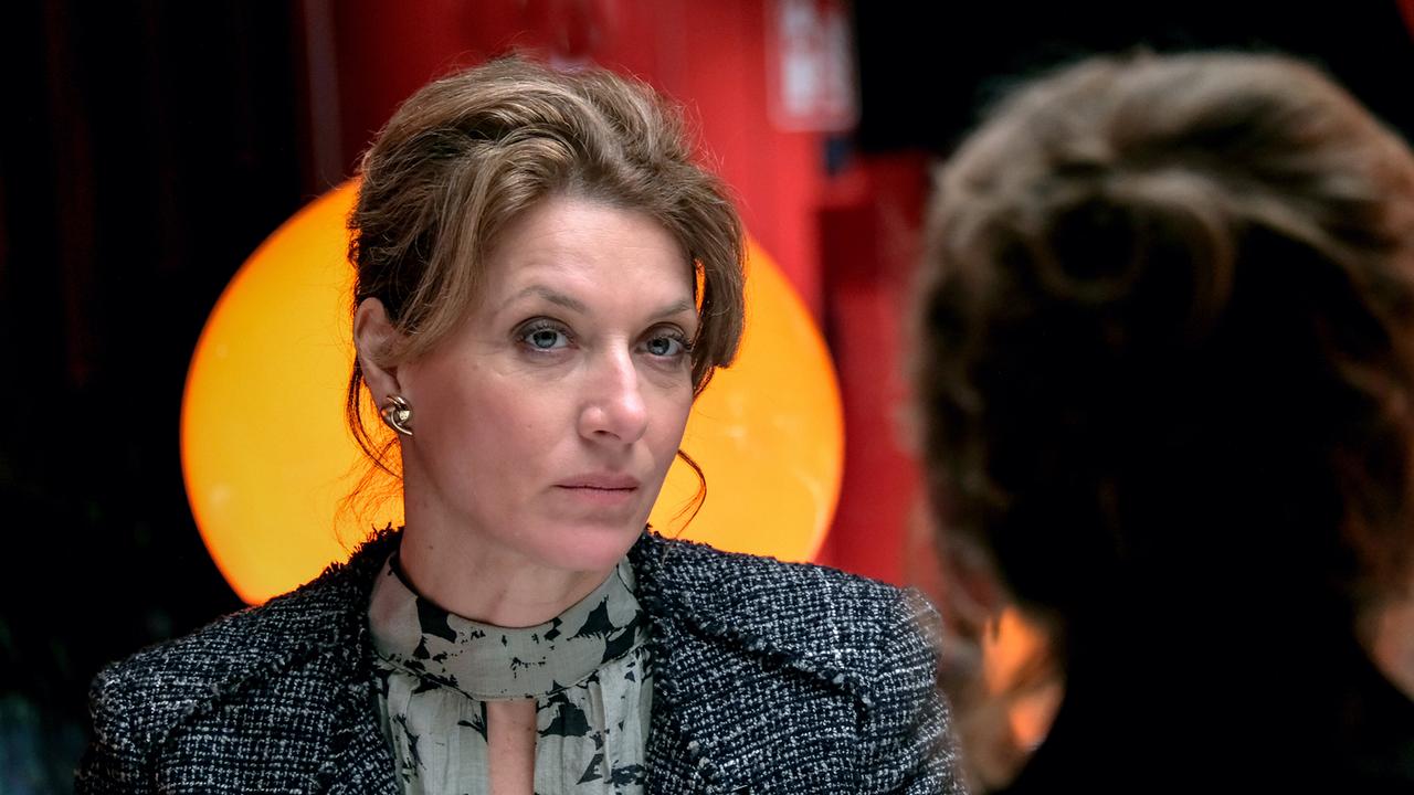 Karin Biederstädt sitzt an einem Tisch in einem Lokal und spricht mit Constanze Laux, die ihr gegenüber sitzt.