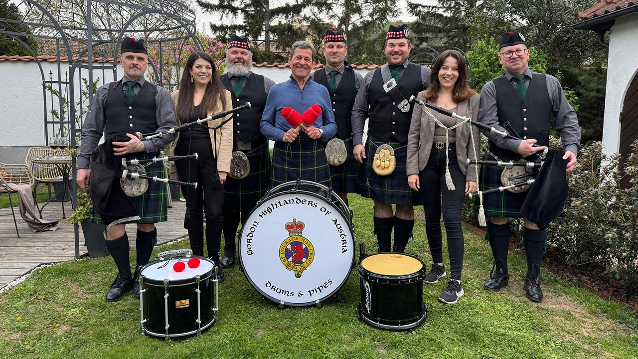 Franz Posch und der Highlander-Verein in Kilt-Uniformen und die Winzerinnen Anna und Lisa posieren gemeinsam im Garten mit Dudelsäcken und Trommeln.