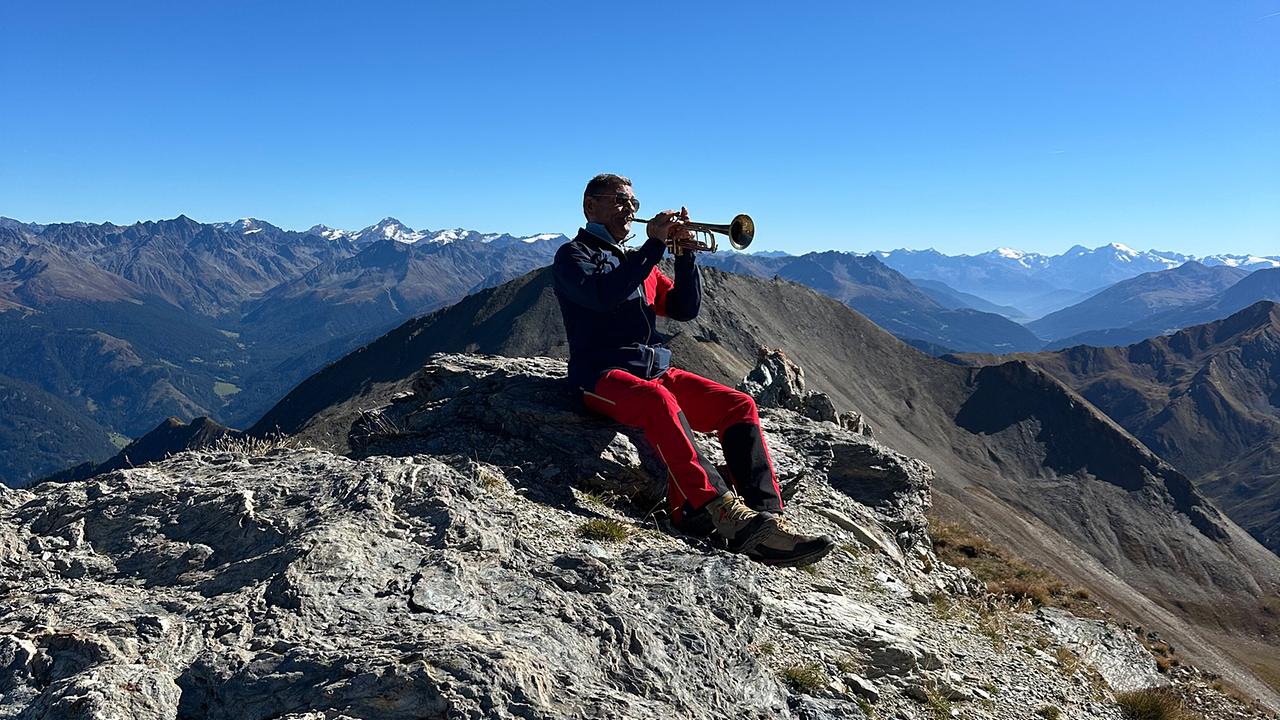 © ORF/Landesstudio Tirol Franz Posch spielt Trompete auf einem felsigen Gipfel in der beeindruckenden Berglandschaft von Serfaus-Fiss-Ladis.