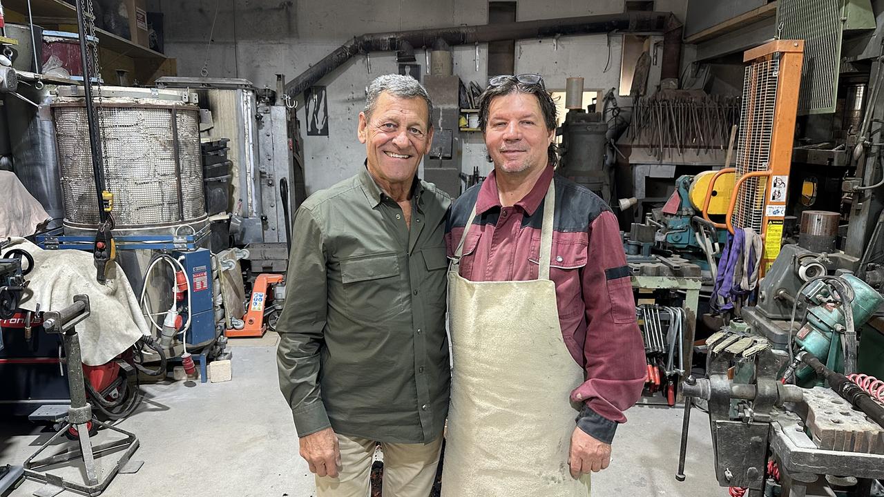 © ORF/Landesstudio Tirol Franz Posch steht mit dem Serfauser Künstler Walter File lächelnd in einer Metallwerkstatt zwischen Maschinen und Werkzeugen.