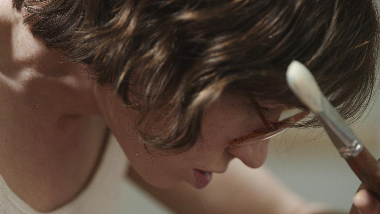 Nahaufnahme des Gesichts und Oberkörpers von Maria Lassnig, während sie mit Pinsel arbeitet.