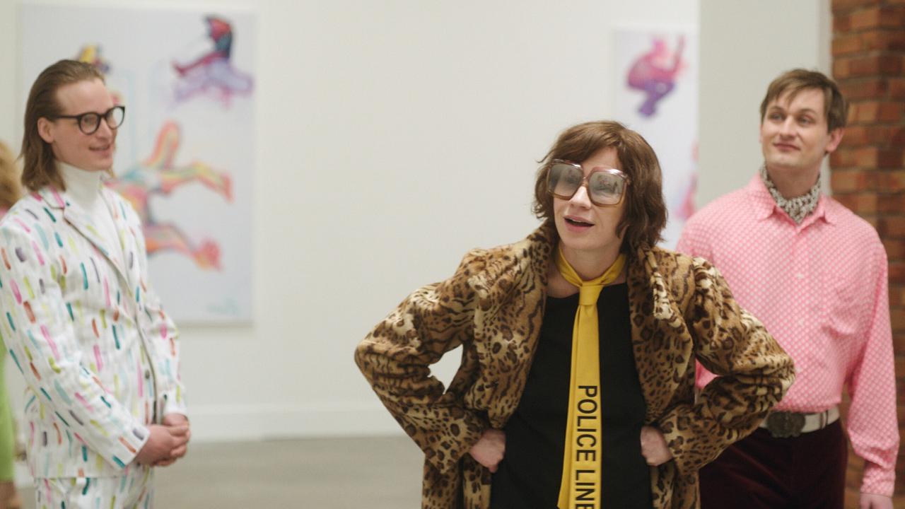 Hans Ulrich Obrist in einem bunten Anzug, Maria Lassnig in einem Leo-Webpelzmantel und Hans-Werner Poschauko stehen in einer Galerie vor großformatigen, farbigen Figurenbildern.