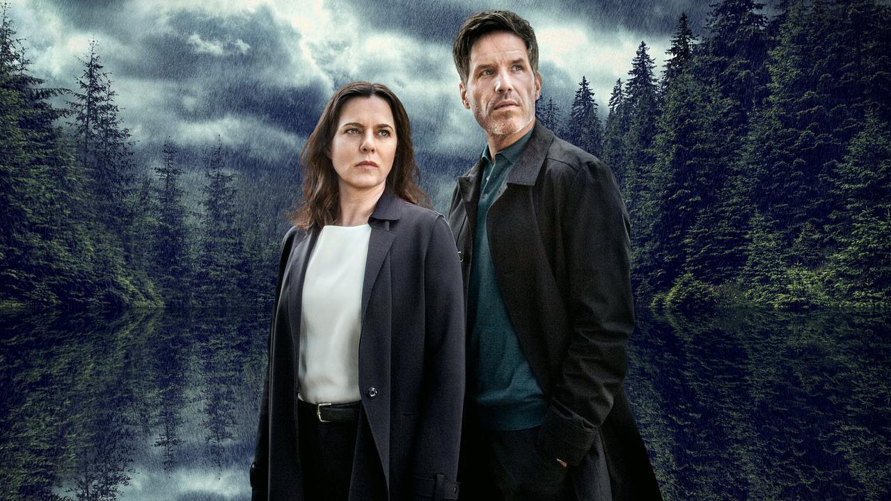 Die Kommissare Pia Sander und Oliver von Bodenstein blicken erst rechts aus dem Bild, dahiter eine Waldkulisse.
