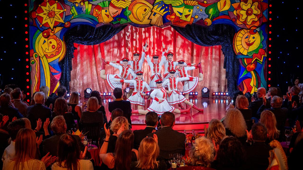 Die Faschingsgilde Völkermarkt in rot-weißen Kostümen formiert sich auf der "Narrisch Guat"-Bühne, während das Publikum applaudiert.