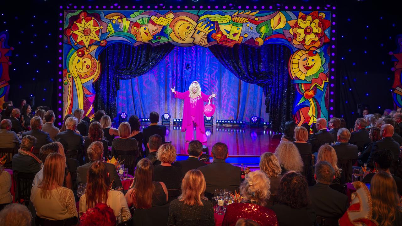 „Chantal“ Claudia Engelmeier im pinken Outfit steht auf der bunt gerahmten "Narrisch guat"-Bühne vor Publikum.