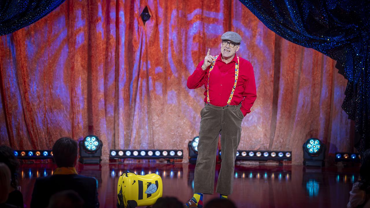 Walter Vaschauner als Scherzinger Sige in rotem Hemd und Cordhose mit Hosenträgern steht bei seinem Stück "Positiv bleiben“ auf der "Narrisch guat"-Bühne vor Publikum. 