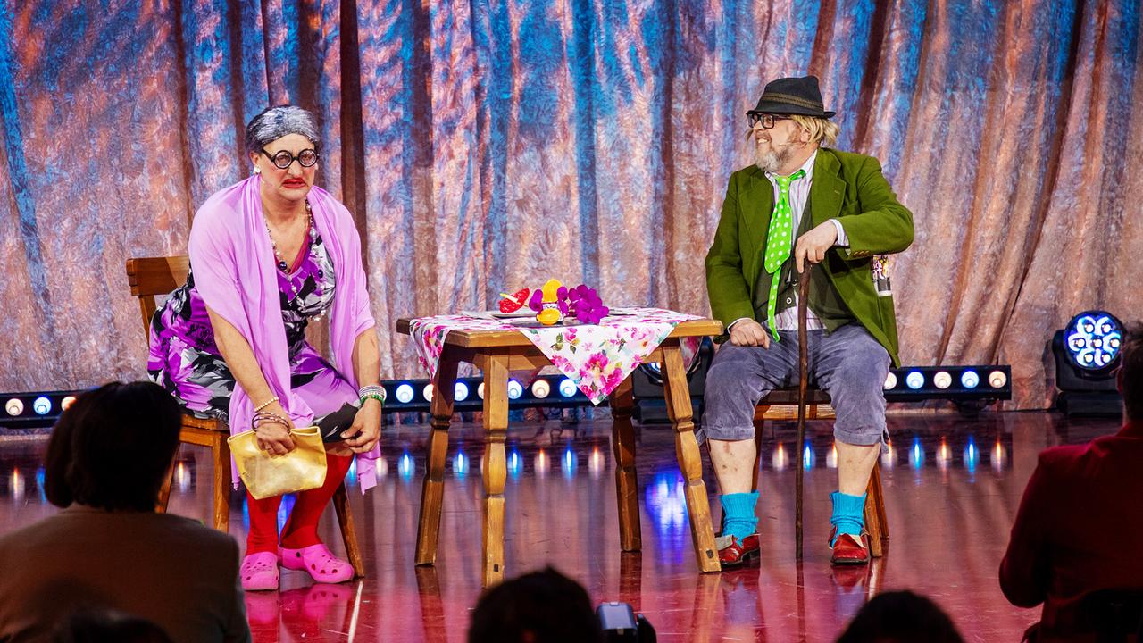 "Der Tschentsche und seine Henriette", Andreas Fischer und Willie Wurzer, sitzen an einem kleinen Tisch und spielen eine humorvolle Szene auf der "Narrisch guat"-Bühne.