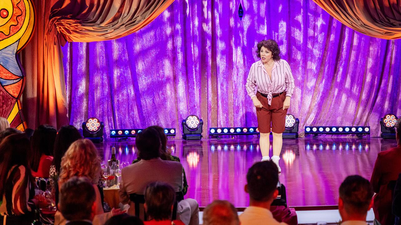 Silvana Kert in Bluse und kurzer Hose spielt eine Szene "Frau Mali in Wien" auf der "Narrisch guat"-Bühne vor Publikum