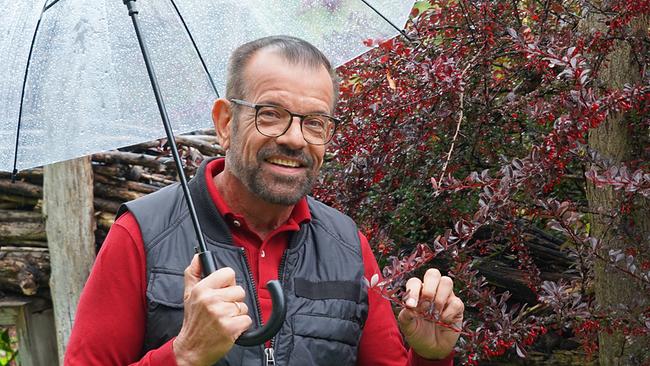Karl Ploberger vor herbstlichem Strauch mit Regenschirm