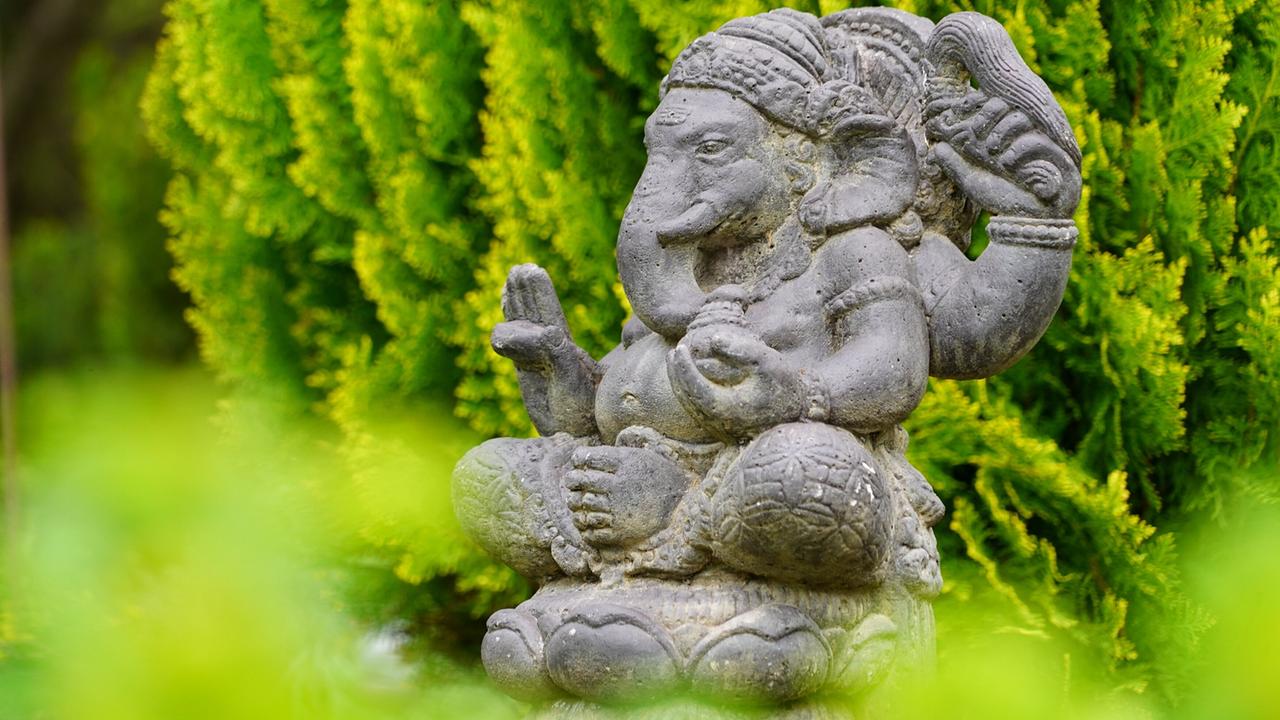 Steinfigur mit Elefantenkopf zwischen dichten grünen Sträuchern 