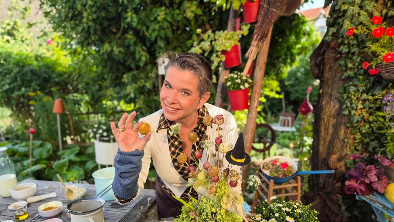 © ORF/Uschi Zezelitsch Uschi Zezelitsch am Gartentisch mit Gewürzschalen und Kräutern, hält Kreuzkümmelsamen in der erhobenen Hand.