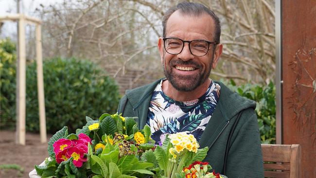 © Leopold Mayrhofer/Natur im Garten Karl Ploberger hält lachend einen Korb mit mehreren blühenden Primeln in der Hand.