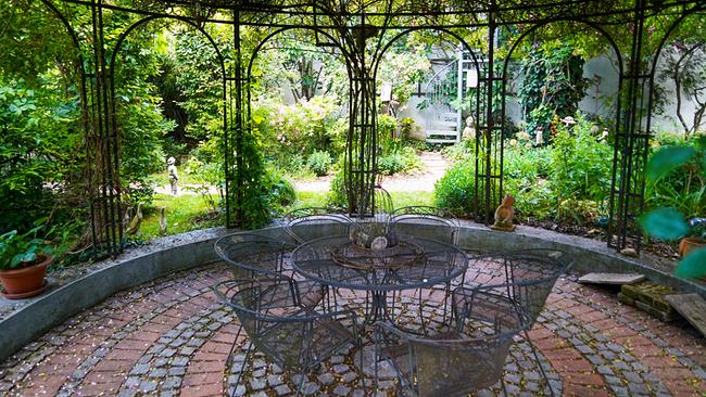 © Leopold Mayrhofer/Natur im Garten Runder Metalltisch mit Metallstühlen unter einem mit Kletterpflanzen bewachsenen, runden Pergolagerüst.