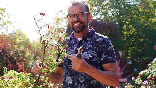 Karl Ploberger präsentiert österreichische Pflanze mit roten Beeren und Gartenschere im Garten.