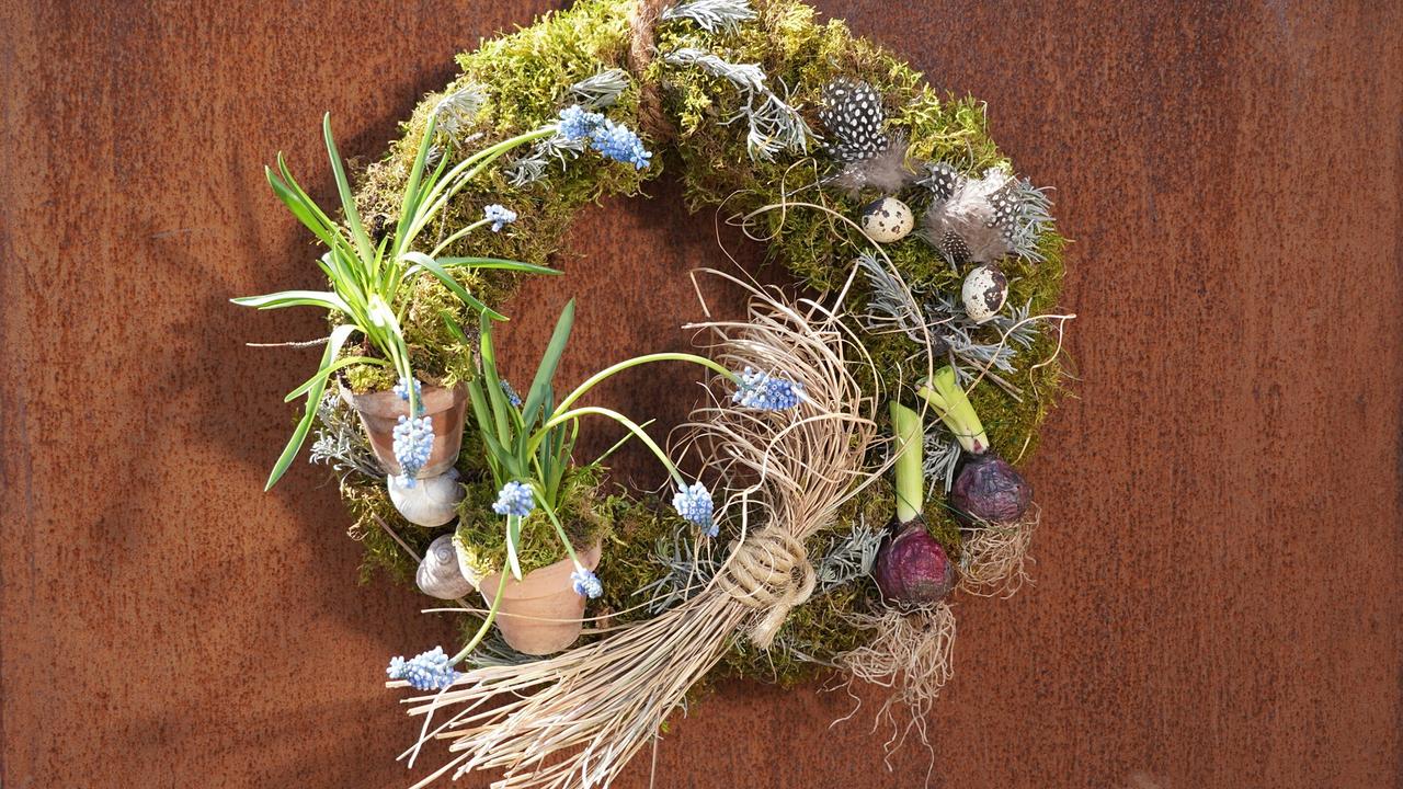 Deko-Kranz aus Moos mit kleinen Tontöpfen, Traubehyazinthen, Federn und Eiern.