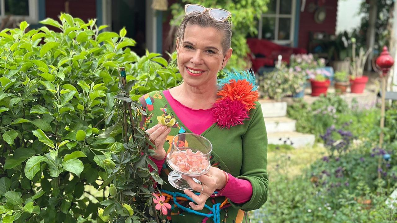 Uschi Zezelitsch hält eine Glasschale mit ihren Fruchtgummis in einem Garten.